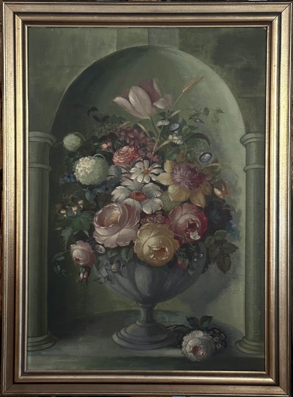 A framed classical floral still life painting depicting a colourful bouquet of flowers inside a stone urn set within an arched architectural niche.