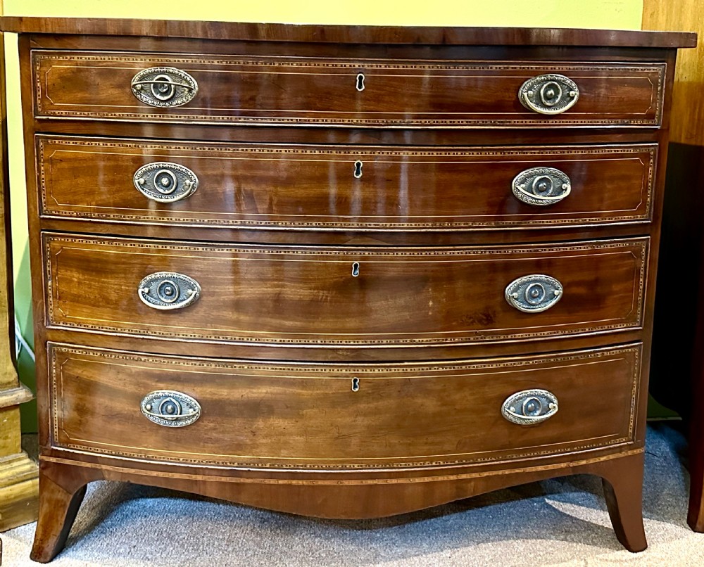 A Georgian mahogany bow front chest of drawers featuring four graduated drawers with oval brass handles and fine stringing inlay, raised on splayed bracket feet.