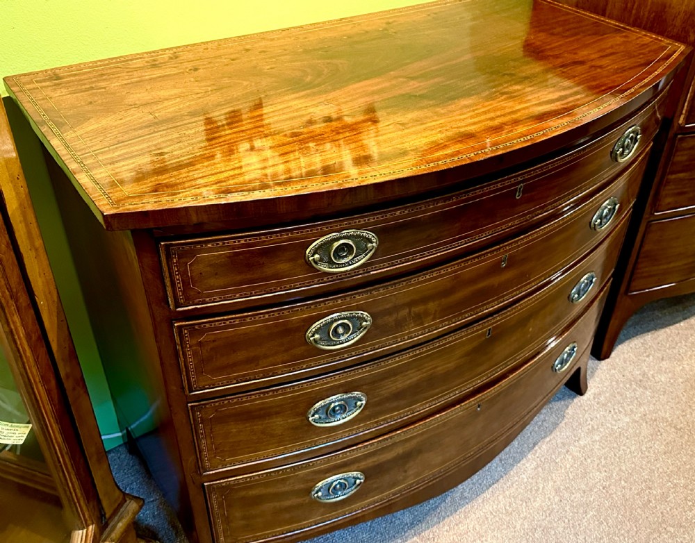 A Georgian mahogany bow front chest of drawers featuring four graduated drawers with oval brass handles and fine stringing inlay, raised on splayed bracket feet. View II