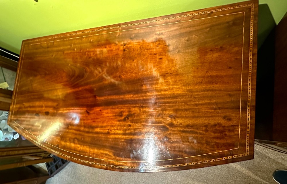 A Georgian mahogany bow front chest of drawers featuring four graduated drawers with oval brass handles and fine stringing inlay, raised on splayed bracket feet. View VI