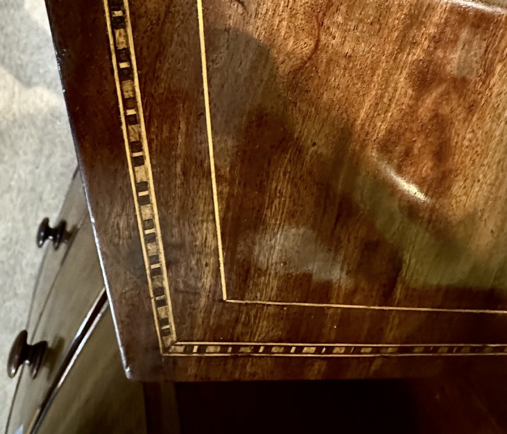 A Georgian mahogany bow front chest of drawers featuring four graduated drawers with oval brass handles and fine stringing inlay, raised on splayed bracket feet. View VII