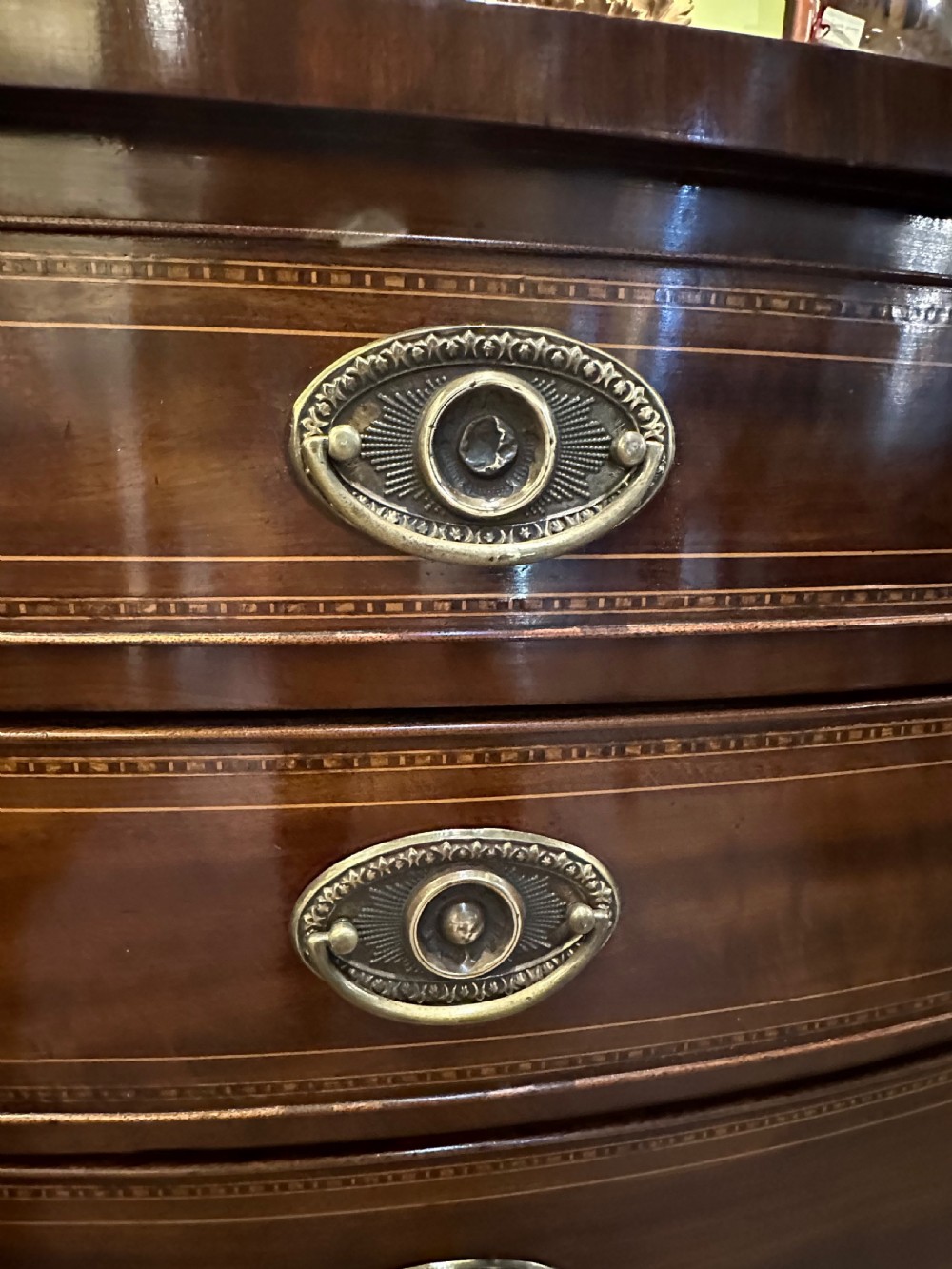 A Georgian mahogany bow front chest of drawers featuring four graduated drawers with oval brass handles and fine stringing inlay, raised on splayed bracket feet. View VIII