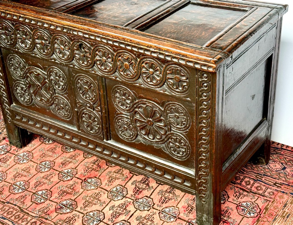 A dark oak coffer featuring three panelled front sections with carved rosette motifs and a carved top frieze. View II