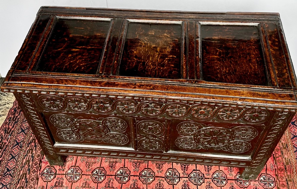 A dark oak coffer featuring three panelled front sections with carved rosette motifs and a carved top frieze. View III