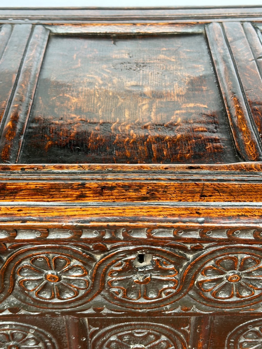 A dark oak coffer featuring three panelled front sections with carved rosette motifs and a carved top frieze. View V