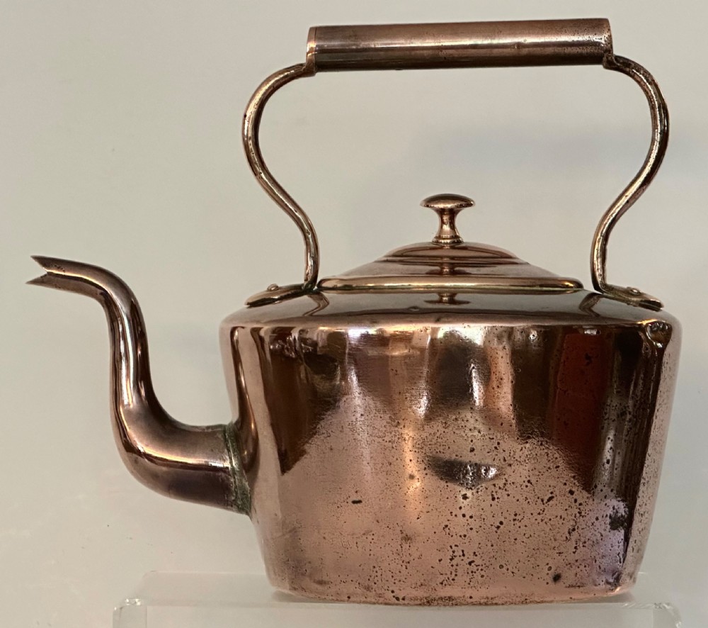 An antique copper tea kettle featuring a gooseneck spout, stationary overhead handle, and fitted lid with a central finial.