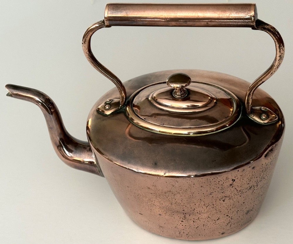 An antique copper tea kettle featuring a gooseneck spout, stationary overhead handle, and fitted lid with a central finial. View II
