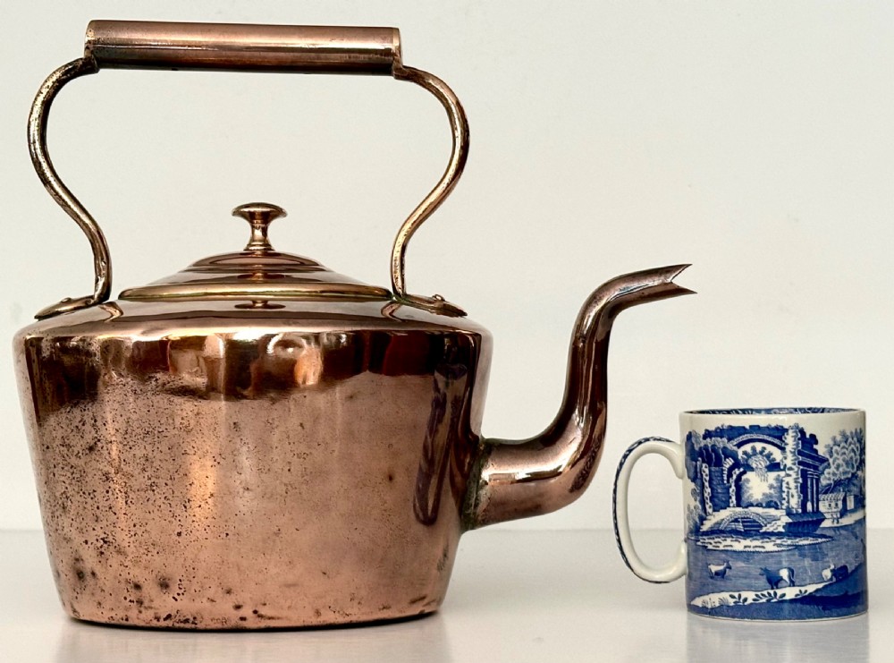 An antique copper tea kettle featuring a gooseneck spout, stationary overhead handle, and fitted lid with a central finial. View VI