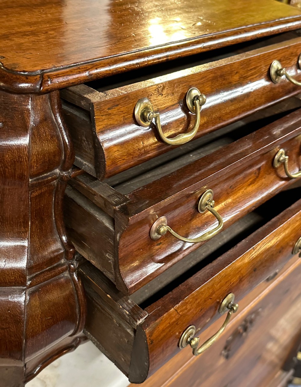 A miniature dark oak Dutch apprentice chest of drawers featuring a bombee front, three drawers with brass drop handles, and carved bracket feet. View VI