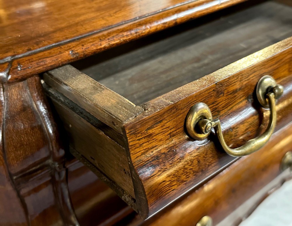 A miniature dark oak Dutch apprentice chest of drawers featuring a bombee front, three drawers with brass drop handles, and carved bracket feet. View XVI