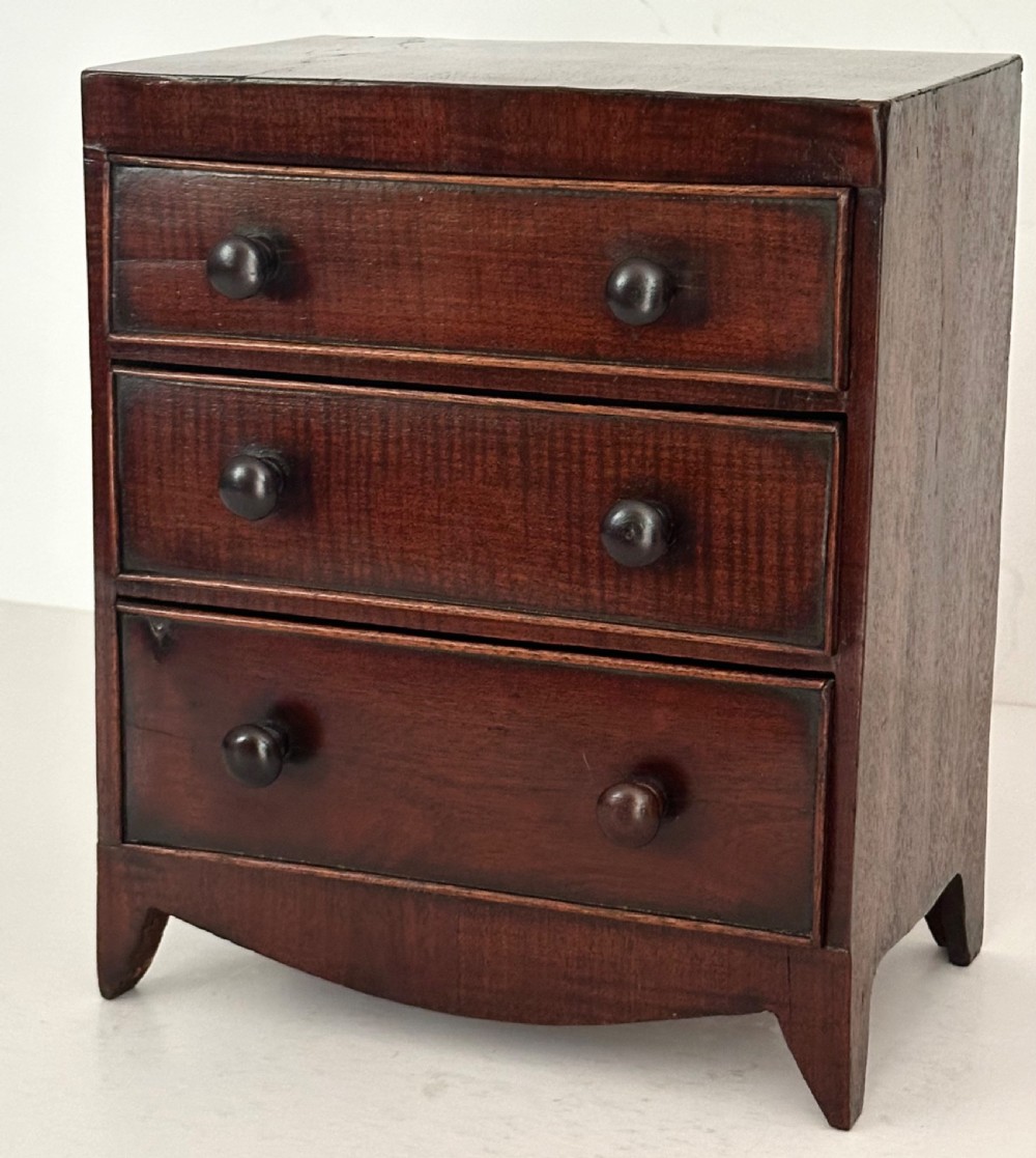 An antique mahogany miniature apprentice chest featuring three drawers with turned knobs and a shaped lower apron.