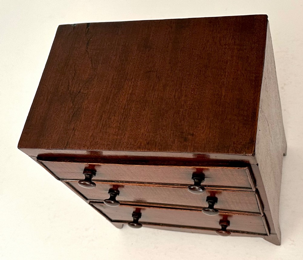 An antique mahogany miniature apprentice chest featuring three drawers with turned knobs and a shaped lower apron. View IV