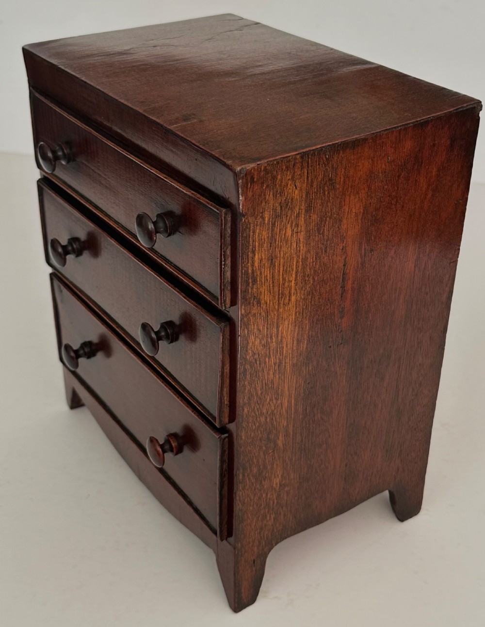 An antique mahogany miniature apprentice chest featuring three drawers with turned knobs and a shaped lower apron. View VI