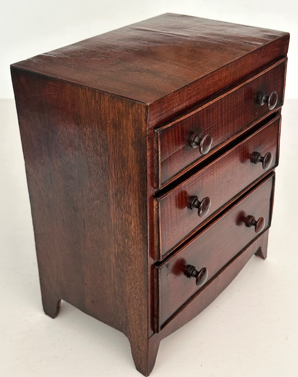 An antique mahogany miniature apprentice chest featuring three drawers with turned knobs and a shaped lower apron. View VII