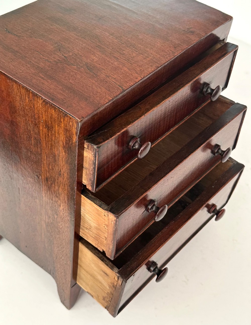 An antique mahogany miniature apprentice chest featuring three drawers with turned knobs and a shaped lower apron. View IX