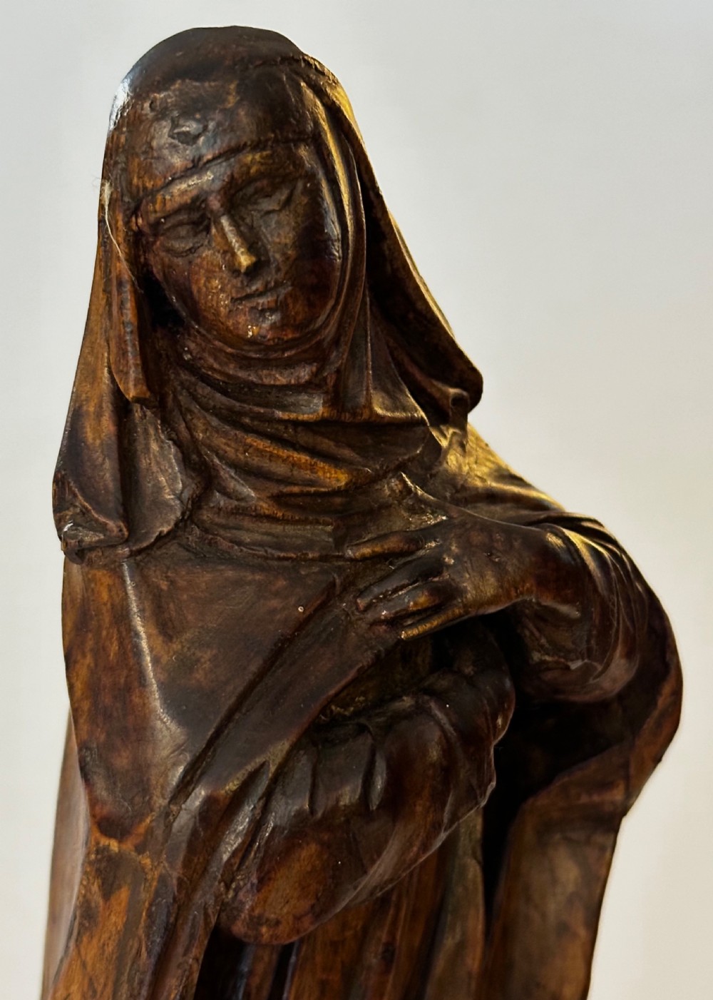 A dark carved wood statue depicting a veiled female religious saint with draped clothing on a faceted wooden base. View IV