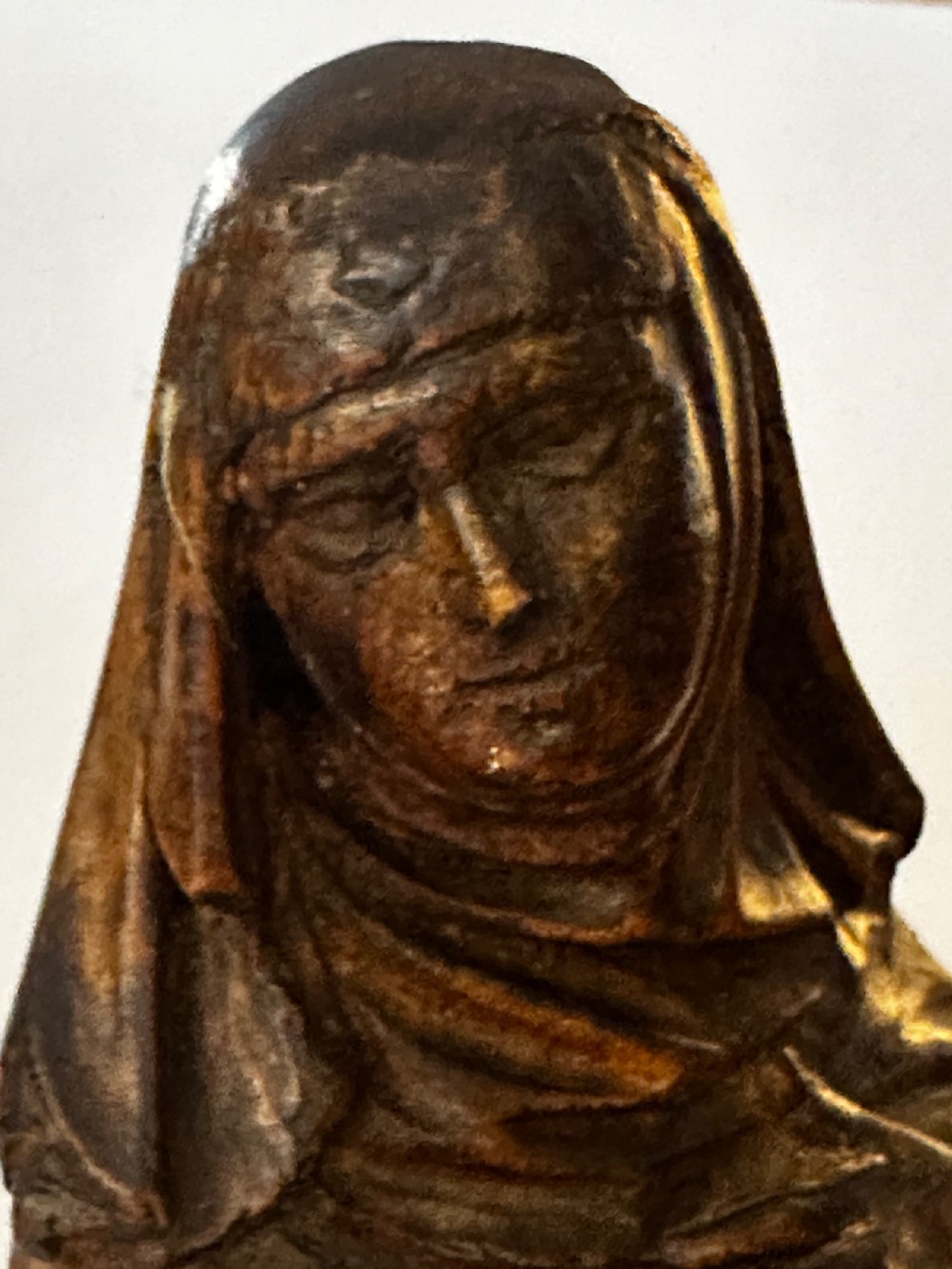 A dark carved wood statue depicting a veiled female religious saint with draped clothing on a faceted wooden base. View V