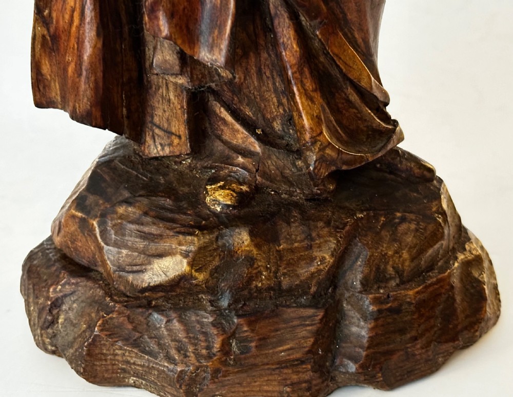A dark carved wood statue depicting a veiled female religious saint with draped clothing on a faceted wooden base. View VI
