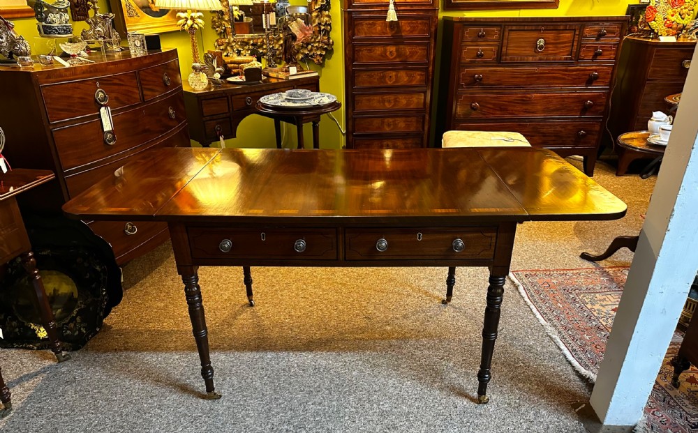 A Regency mahogany and rosewood sofa table featuring two frieze drawers, drop-leaf ends, turned legs, and brass castors. View II