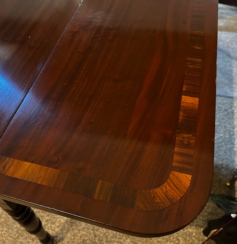 A Regency mahogany and rosewood sofa table featuring two frieze drawers, drop-leaf ends, turned legs, and brass castors. View VIII