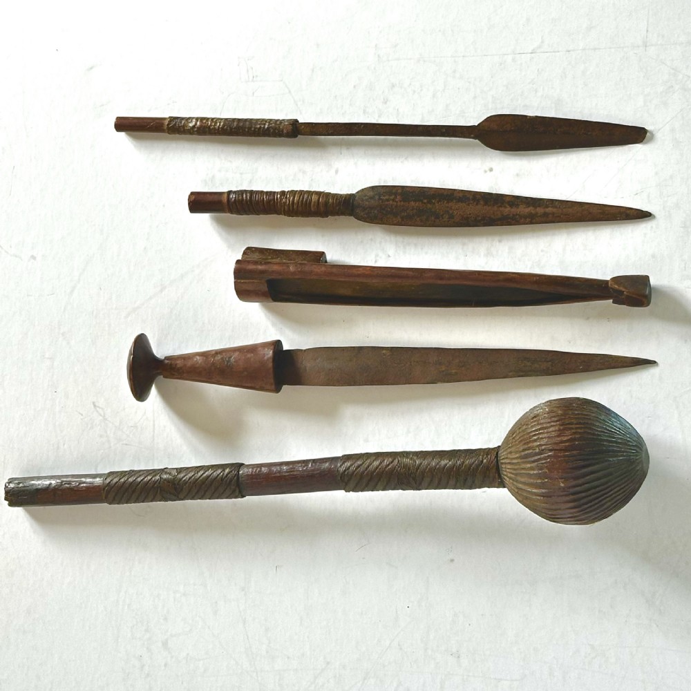 A collection of five traditional Zulu artefacts including a fluted knobkerrie club, a wooden dagger with sheath, and two wire-wrapped spearheads on a plain background.