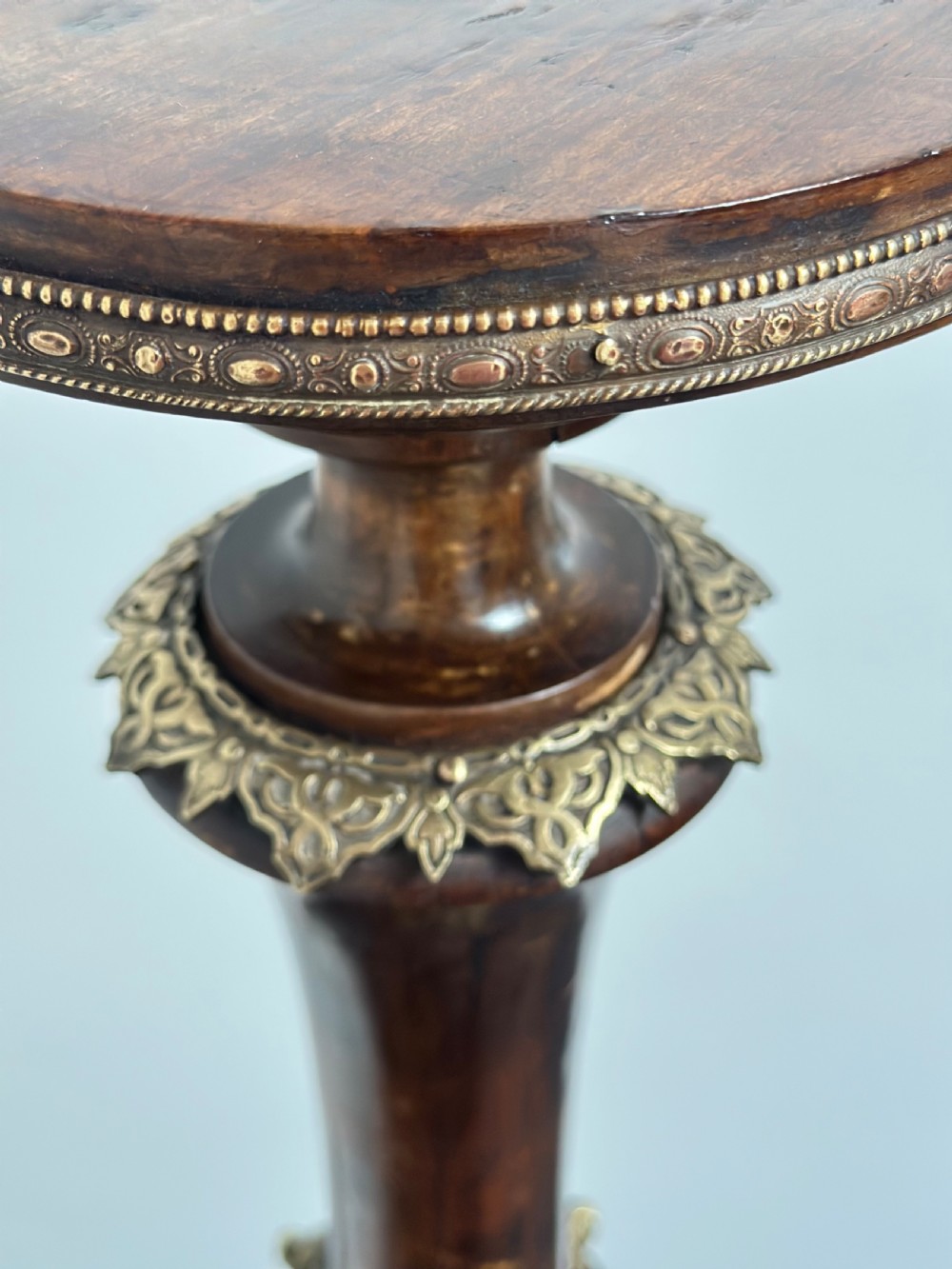 A tall dark hardwood torchere stand featuring a turned central column, brass ormolu mounts, circular top, and a tripod base. View VII