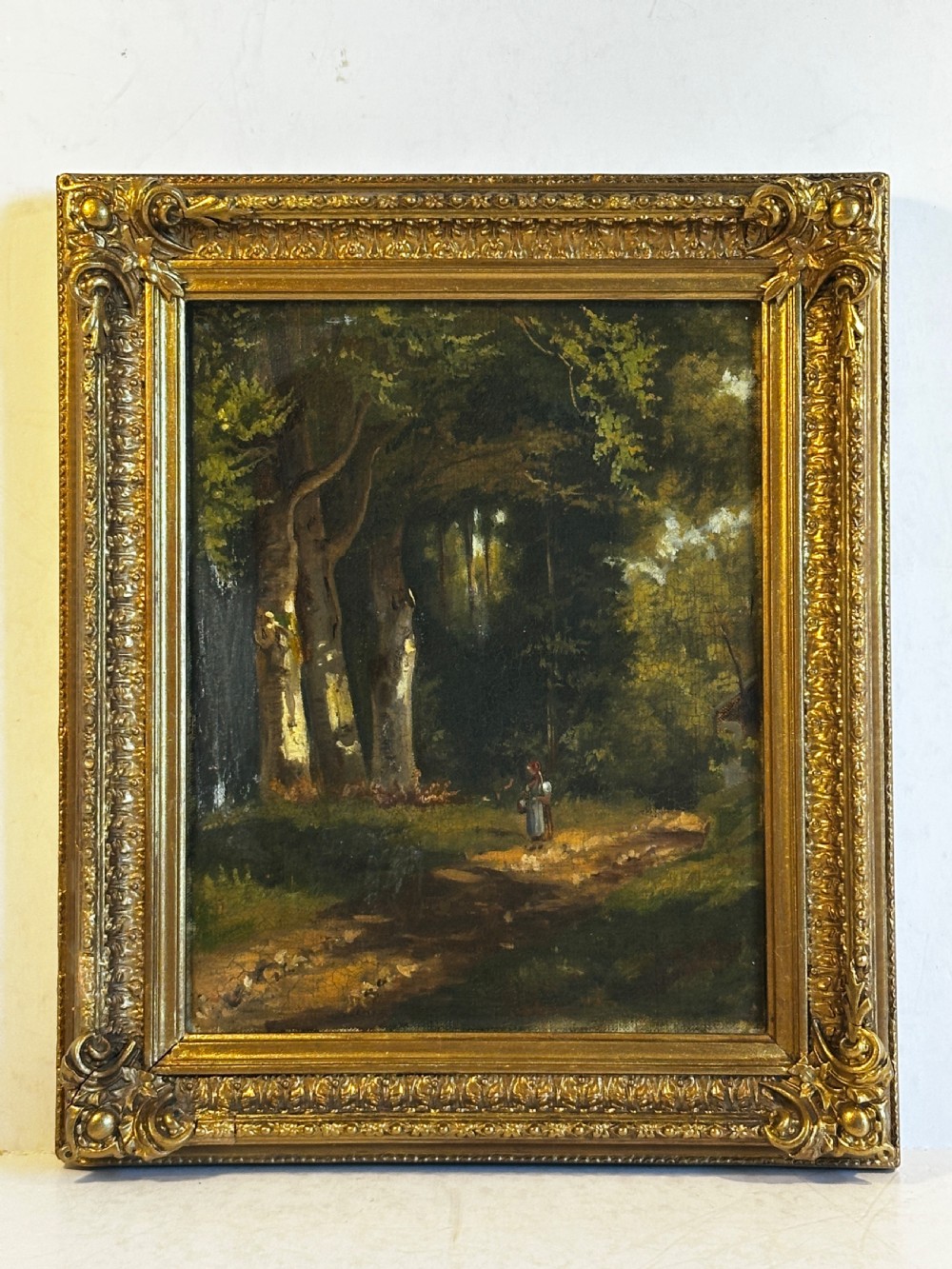 An antique oil painting on canvas depicting a sunlit woodland path with tall green trees and a small figure, set within an ornate gilded frame. View II