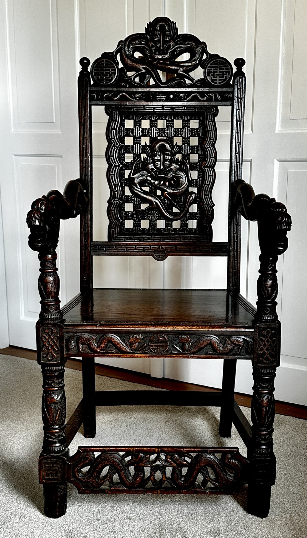 A dark brown carved wood armchair featuring openwork lattice panels, carved dragon motifs on the backrest, apron, and stretchers, and carved dragon heads forming the armrests.