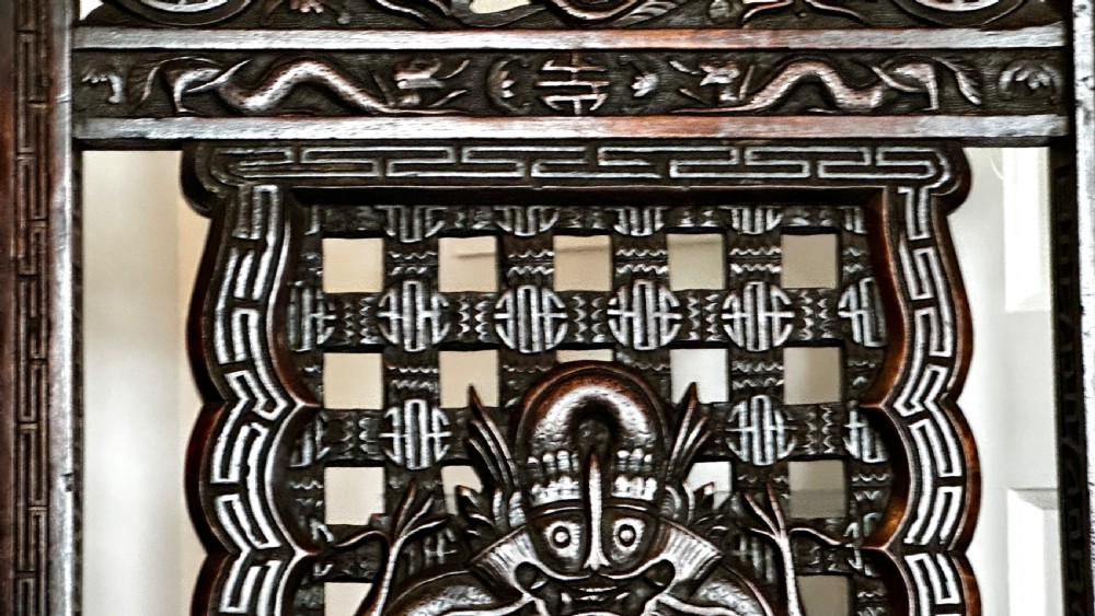 A dark brown carved wood armchair featuring openwork lattice panels, carved dragon motifs on the backrest, apron, and stretchers, and carved dragon heads forming the armrests. View III