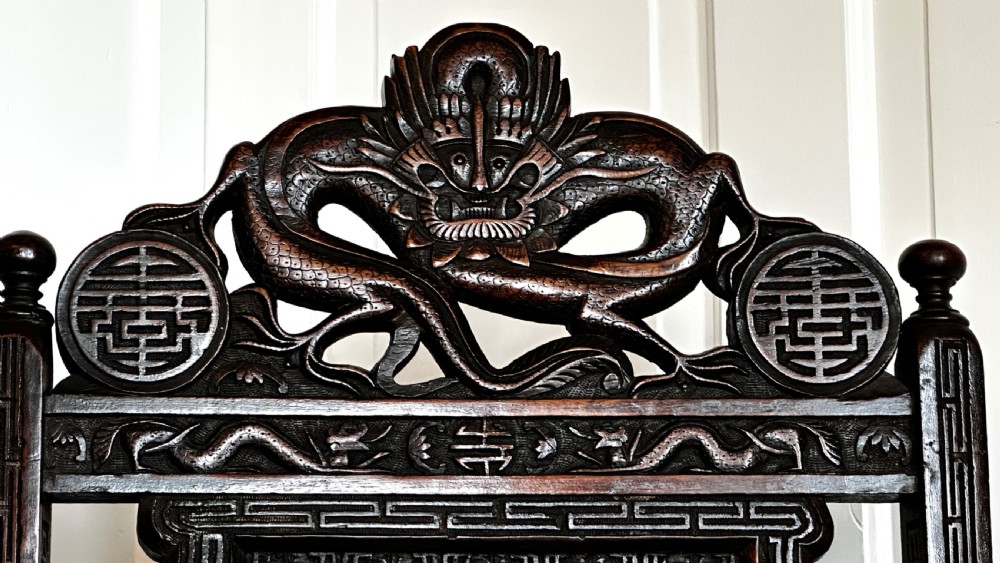 A dark brown carved wood armchair featuring openwork lattice panels, carved dragon motifs on the backrest, apron, and stretchers, and carved dragon heads forming the armrests. View IV