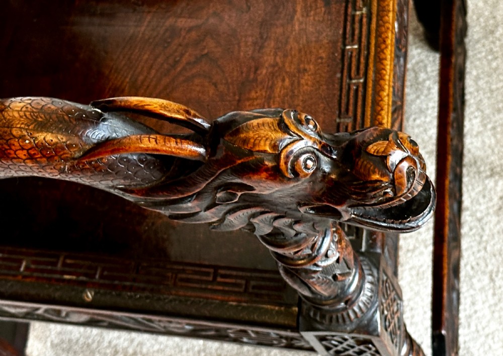A dark brown carved wood armchair featuring openwork lattice panels, carved dragon motifs on the backrest, apron, and stretchers, and carved dragon heads forming the armrests. View IX