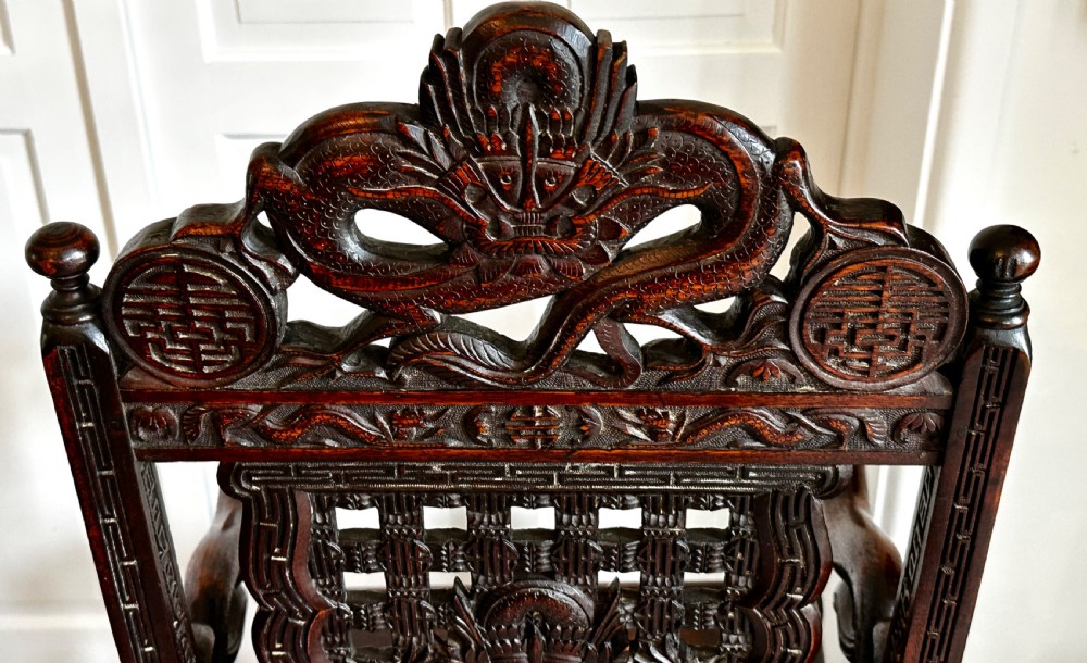 A dark brown carved wood armchair featuring openwork lattice panels, carved dragon motifs on the backrest, apron, and stretchers, and carved dragon heads forming the armrests. View XII