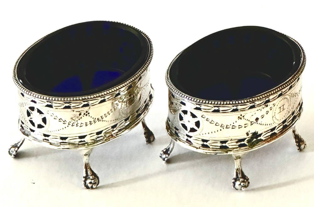 A pair of oval Georgian sterling silver open salt cellars with pierced swags, claw feet, and removable cobalt blue glass liners.