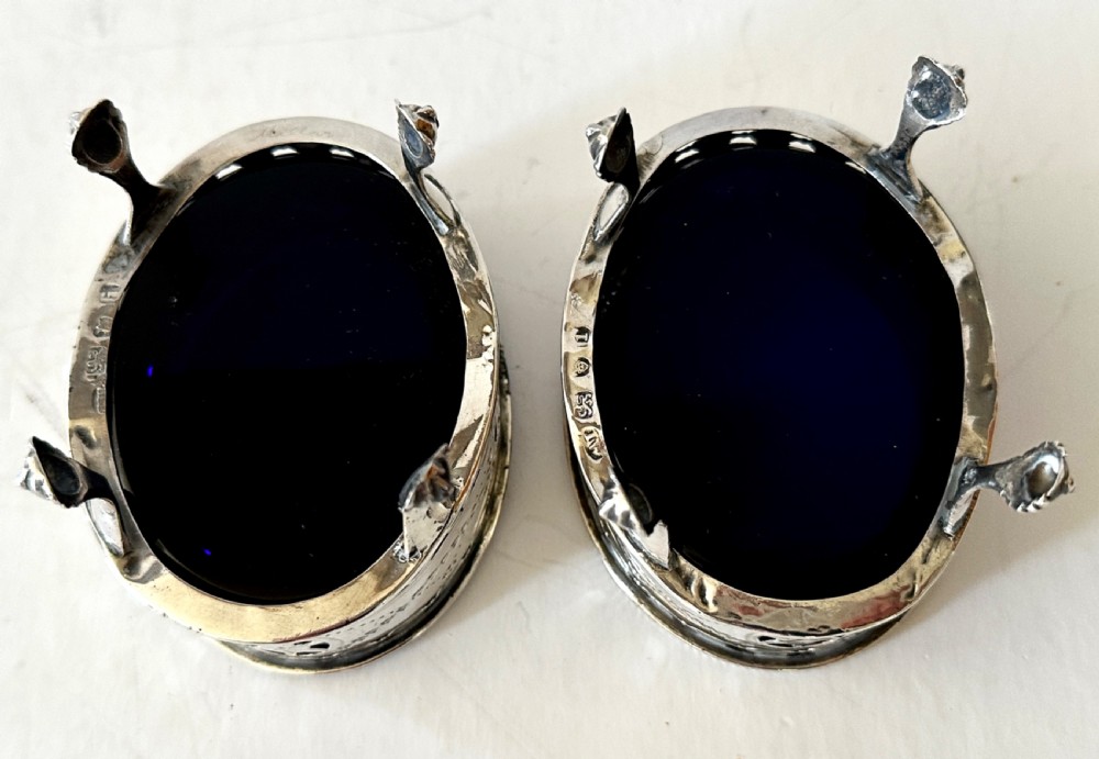A pair of oval Georgian sterling silver open salt cellars with pierced swags, claw feet, and removable cobalt blue glass liners. View VI