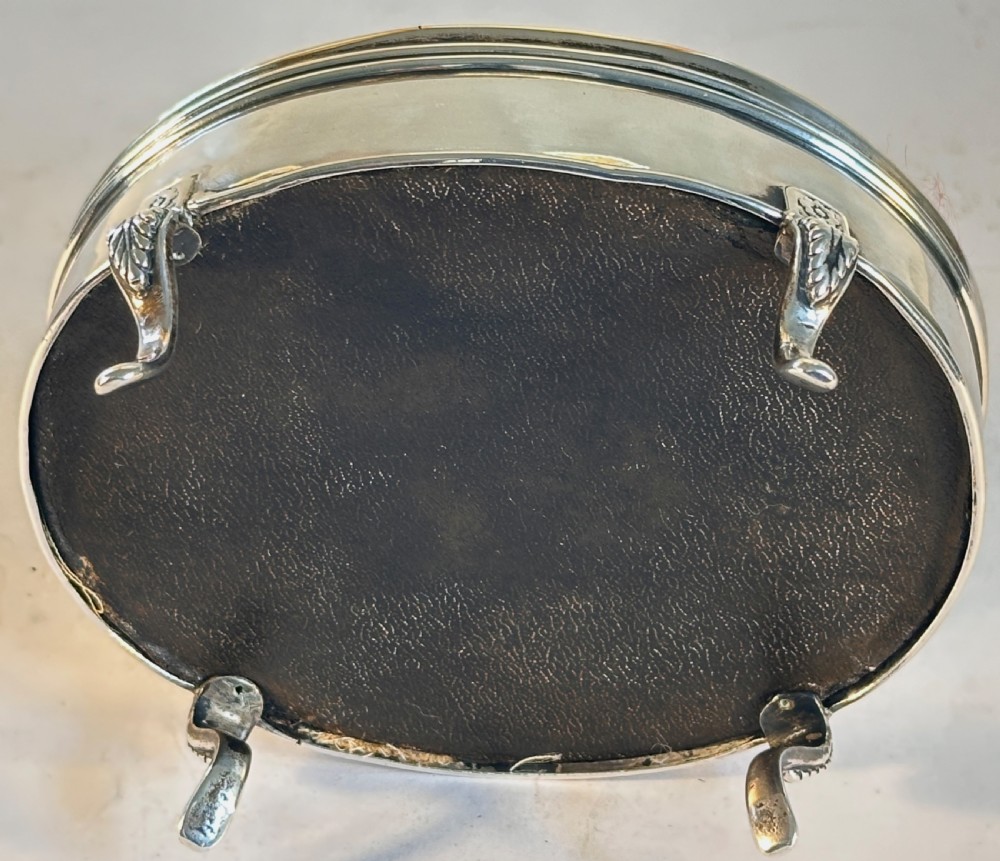 An oval sterling silver jewellery box raised on four small legs, featuring a dark brown tortoiseshell lid inlaid with silver swags and ribbon motifs. View VI