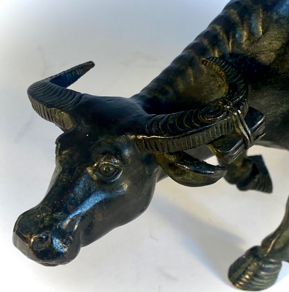 A dark patinated bronze sculpture featuring a scholar seated atop a water buffalo while reading an open book. View VI