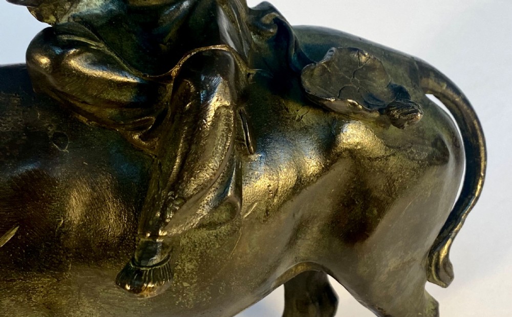 A dark patinated bronze sculpture featuring a scholar seated atop a water buffalo while reading an open book. View VII