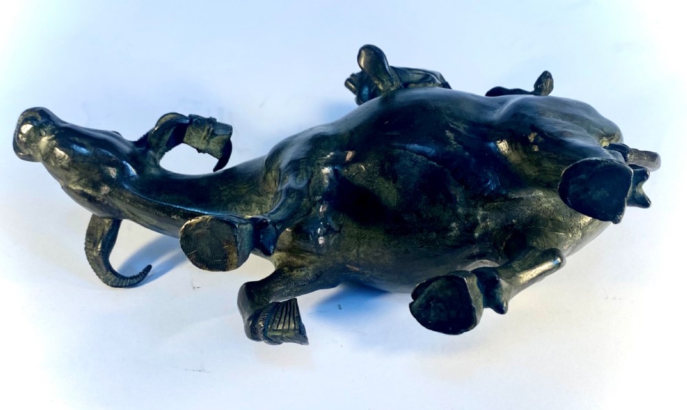 A dark patinated bronze sculpture featuring a scholar seated atop a water buffalo while reading an open book. View IX