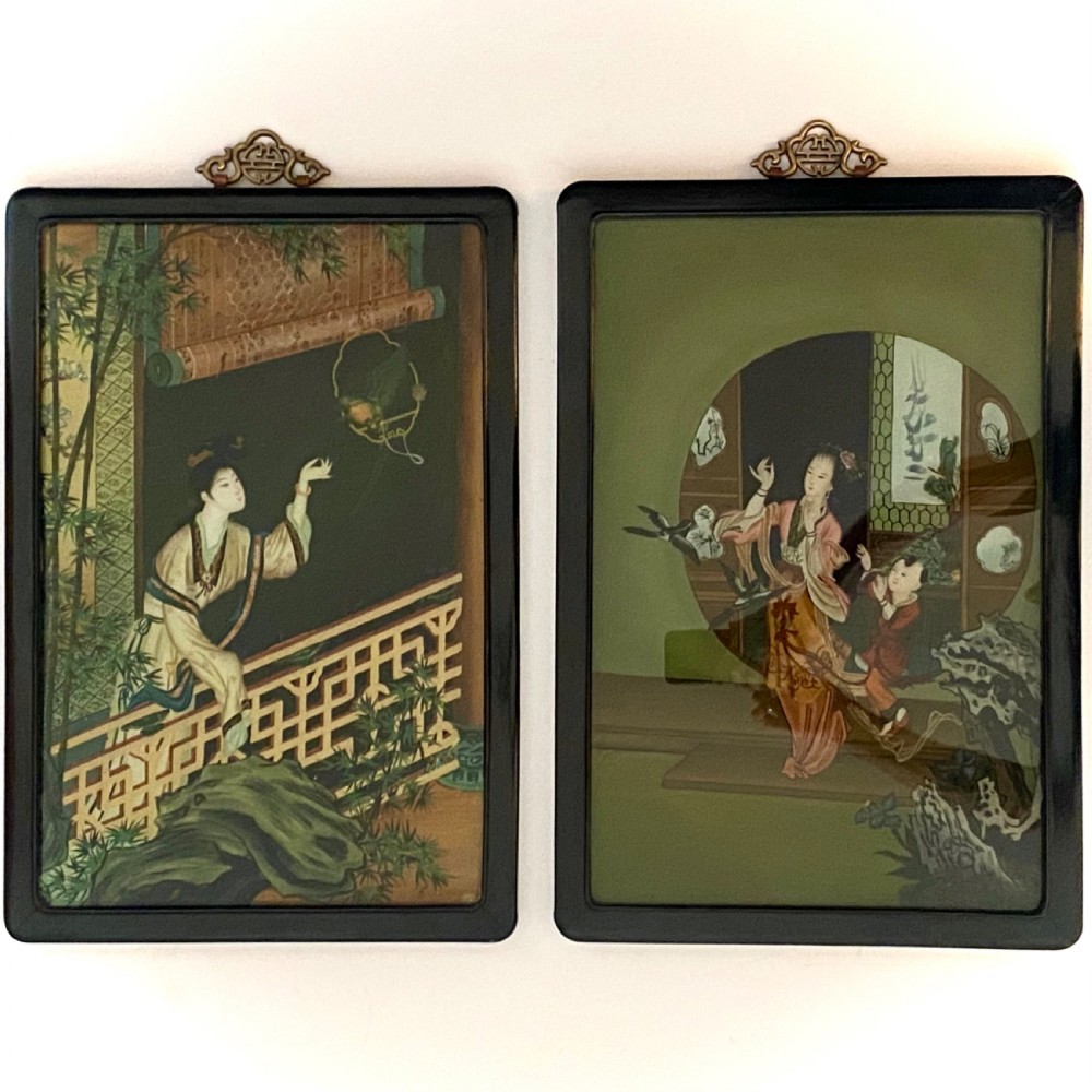 A pair of rectangular reverse glass paintings depicting Chinese figures in architectural settings framed in black lacquer with decorative brass hanging mounts.