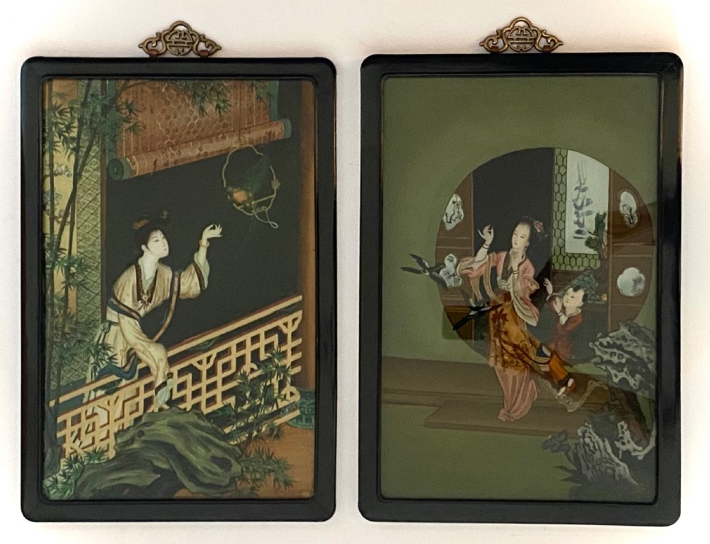 A pair of rectangular reverse glass paintings depicting Chinese figures in architectural settings framed in black lacquer with decorative brass hanging mounts. View II