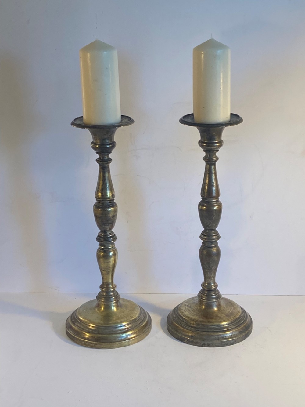 A pair of bronze church pricket candlesticks featuring turned baluster stems, circular stepped bases, drip trays, and central spikes. View II