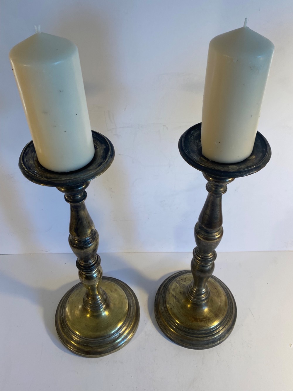 A pair of bronze church pricket candlesticks featuring turned baluster stems, circular stepped bases, drip trays, and central spikes. View III