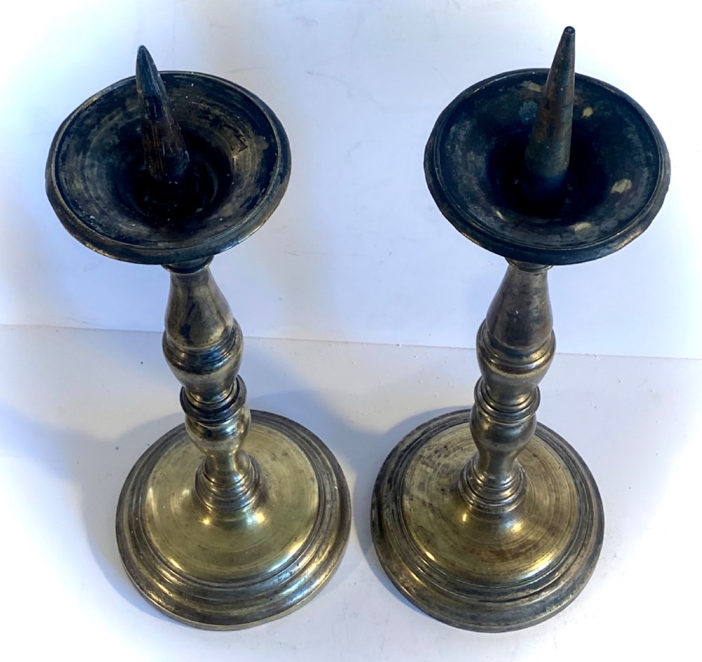 A pair of bronze church pricket candlesticks featuring turned baluster stems, circular stepped bases, drip trays, and central spikes. View IV