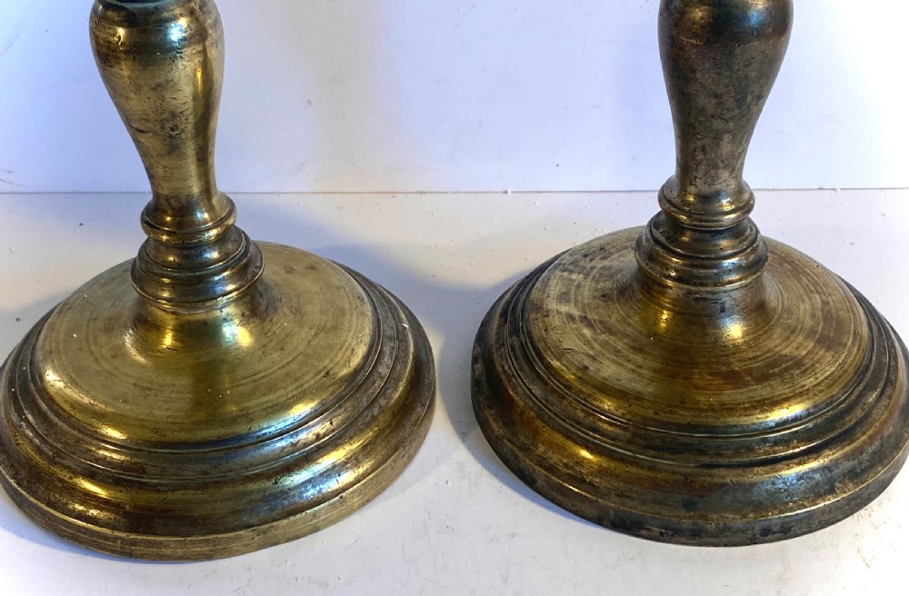 A pair of bronze church pricket candlesticks featuring turned baluster stems, circular stepped bases, drip trays, and central spikes. View V