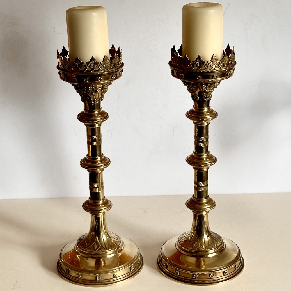 A pair of polished brass ecclesiastical candlesticks featuring pierced coronet galleries, knopped stems, and broad circular bases.