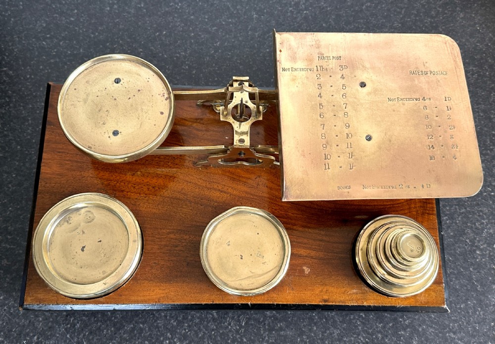 Victorian brass postal scales mounted on a dark mahogany wooden base with turned feet, including a set of nested brass weights. View II