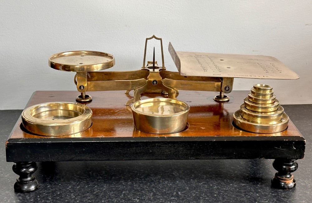 Victorian brass postal scales mounted on a dark mahogany wooden base with turned feet, including a set of nested brass weights. View IV