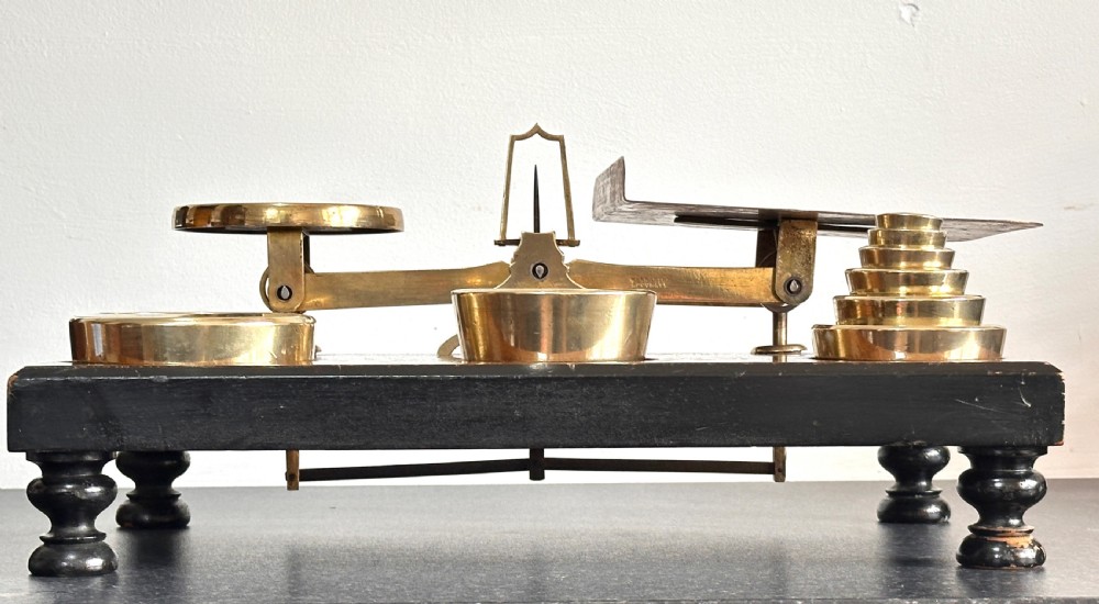 Victorian brass postal scales mounted on a dark mahogany wooden base with turned feet, including a set of nested brass weights. View V