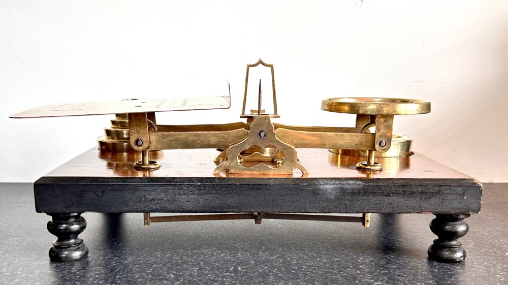 Victorian brass postal scales mounted on a dark mahogany wooden base with turned feet, including a set of nested brass weights. View VII