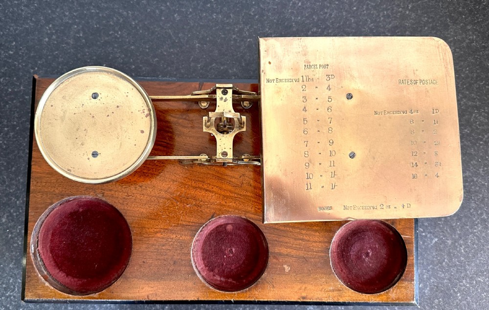 Victorian brass postal scales mounted on a dark mahogany wooden base with turned feet, including a set of nested brass weights. View X